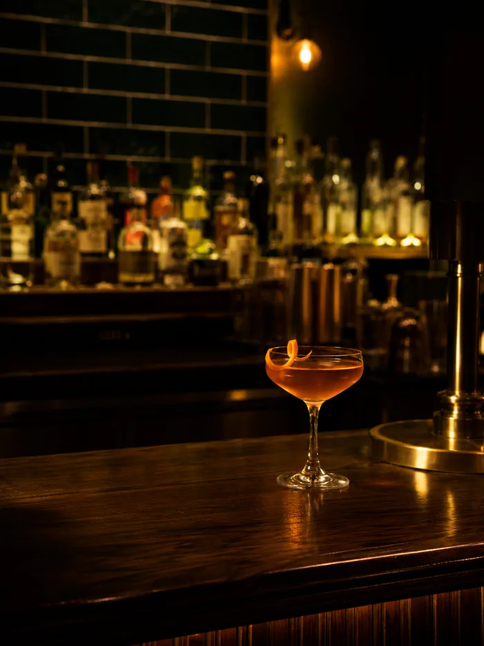 Cocktail på mørk bardisk med flasker i bakgrunnen