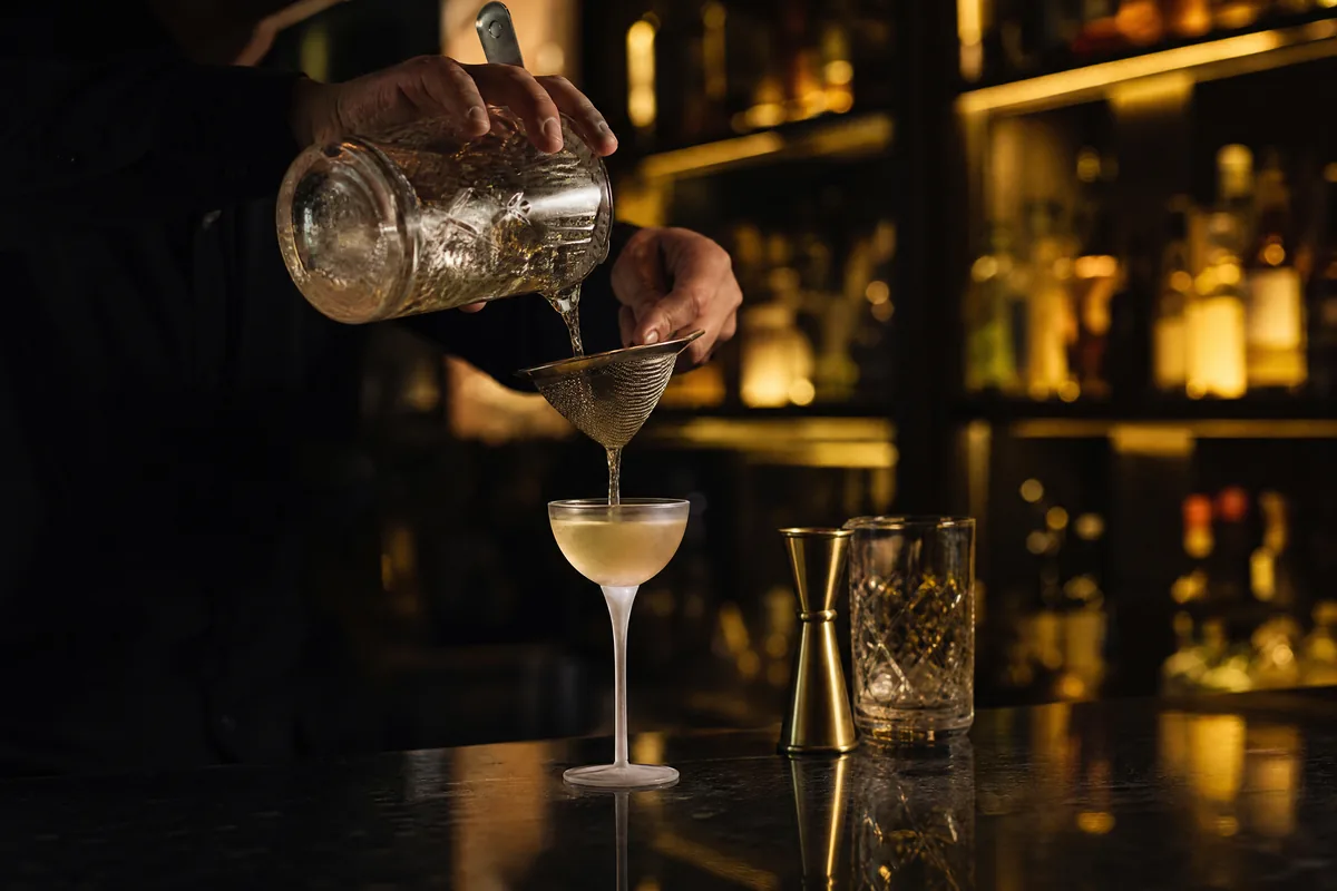 Bartender som siler en drink over i et kjølt glass