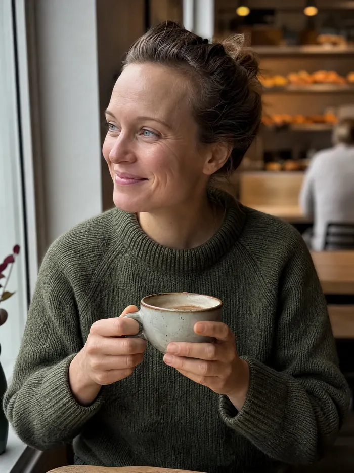 Kvinne med kaffekopp ved vinduet i bakeriet