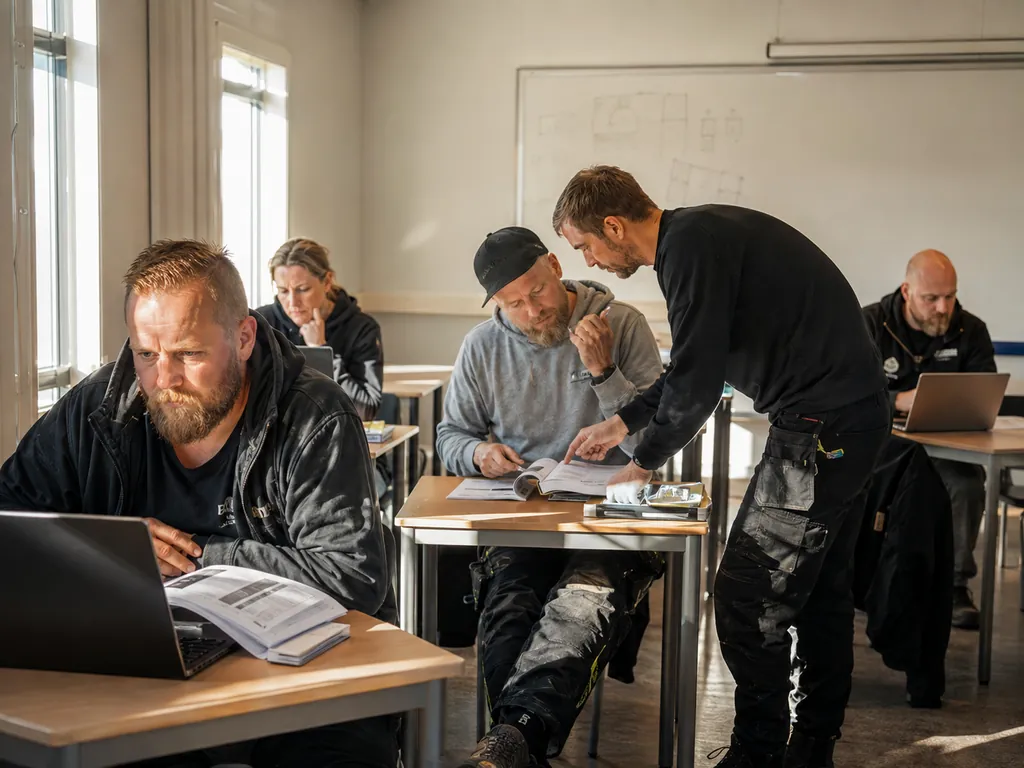 Voksne kursdeltakere jobber med teori ved hver sin pult mens instruktøren veileder