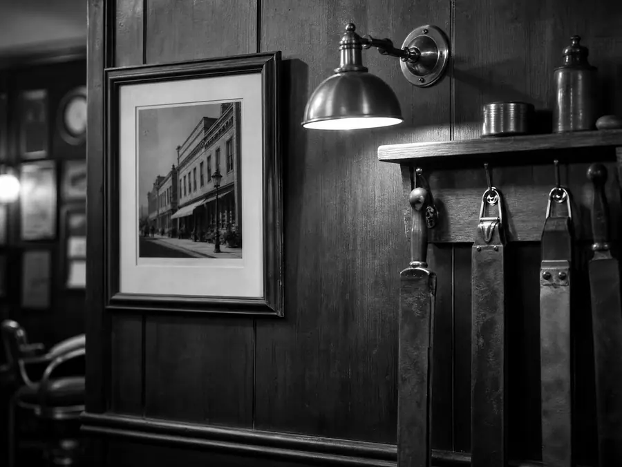 Innramma bilde og messinglampe på den panelte veggen inne i barberstuen